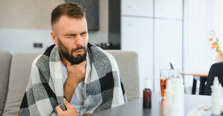 Uomo con coperta e mal di gola con medicinali davanti
