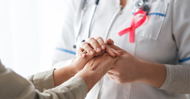 Dottoressa con fiocchetto ottobre rosa che prende le mani della paziente