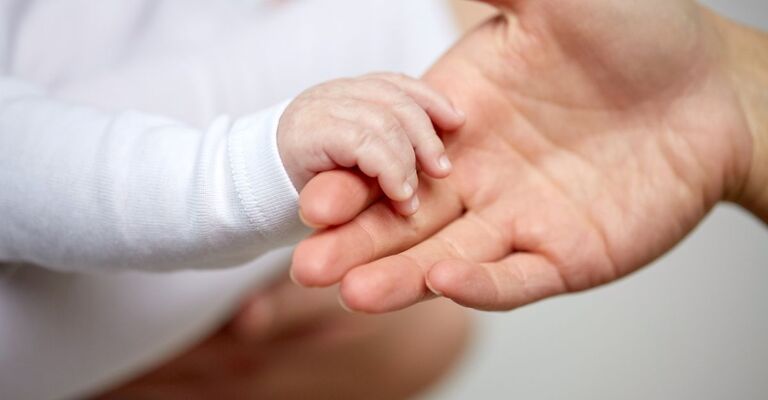 La mano di un genitore che tiene quella di un neonato