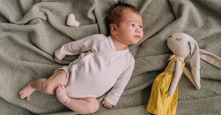 Neonata sdraiata su una coperta con un pupazzo accanto