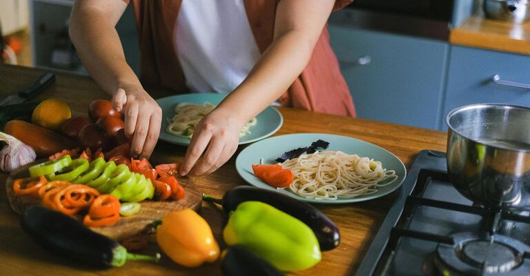 Persona che taglia delle verdure per aggiungerle a due piatti di pasta