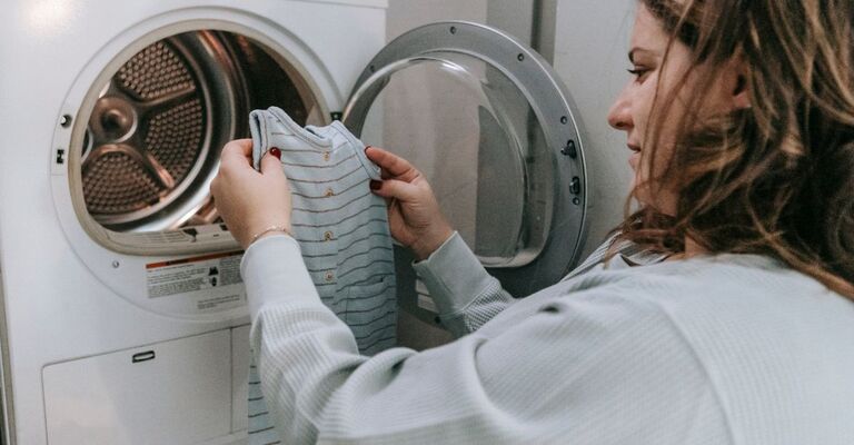 Una donna tira fuori dalla lavatrice dei vestiti da bambino