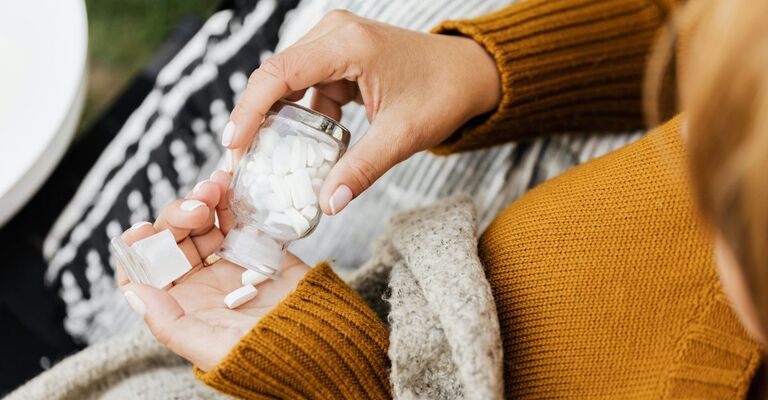 Contenitore con capsule e una mano che le versa nell'altra