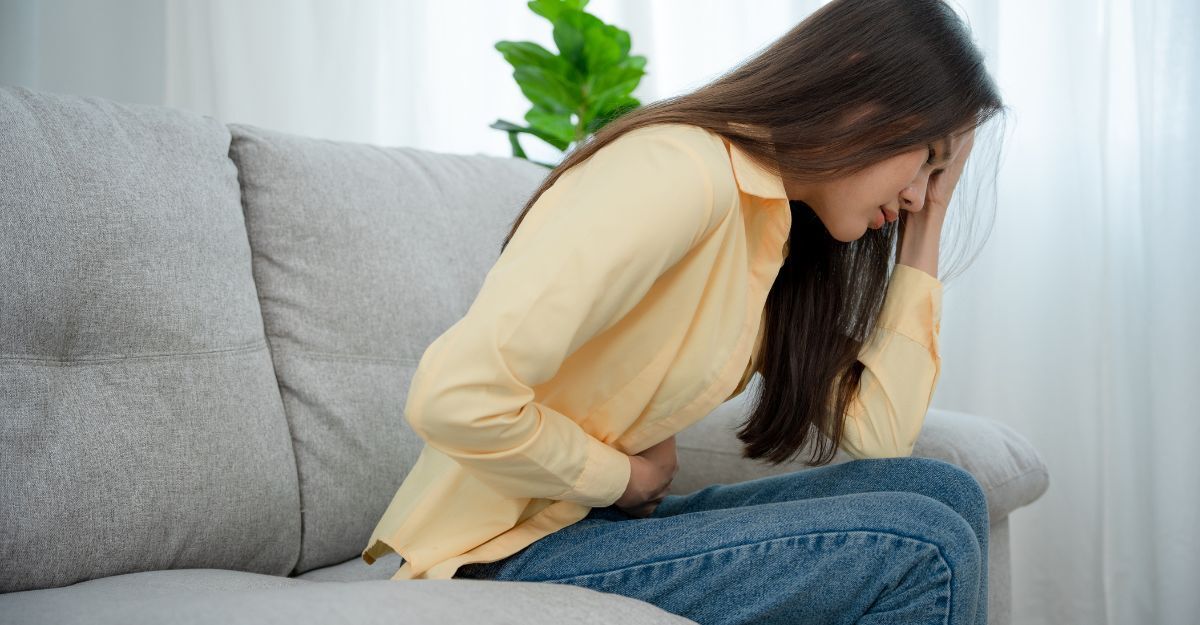 Una ragazza seduta sul divano si tiene la pancia dolorante