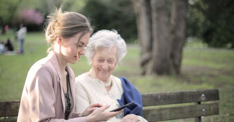 Giovane donna spiega una cosa sul cellulare a un'anziana su una panchina
