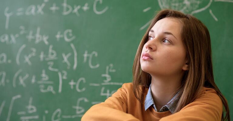 Una ragazzina preoccupata con alle spalle una lavagna su cui è scritto un problema matematico