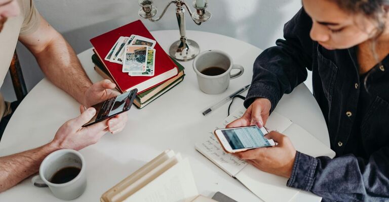 Due persone sedute a un tavolino a casa usano il cellulare