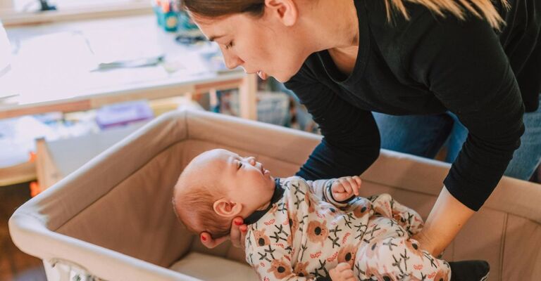 Mamma che mette un neonato nella culla