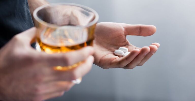 Persona con bicchiere di alcol da una parte e compresse dall'altra