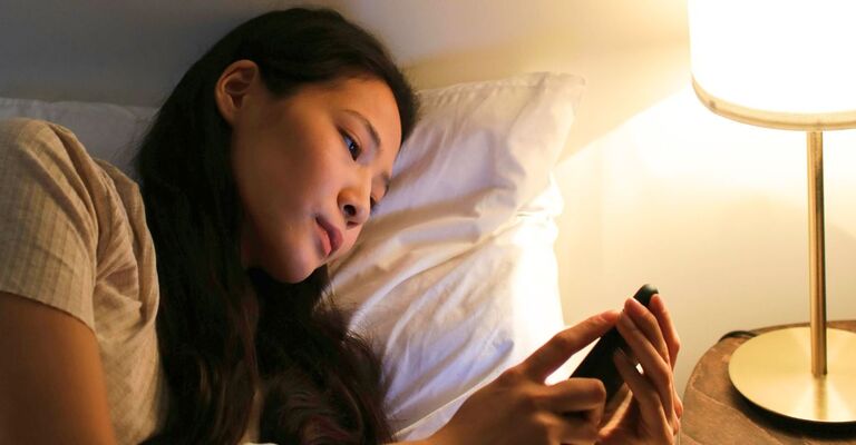 Ragazza sdraiata sul letto di sera che scrolla