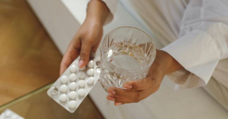 Donna che ha in mano un bicchiere e un blister di integratori