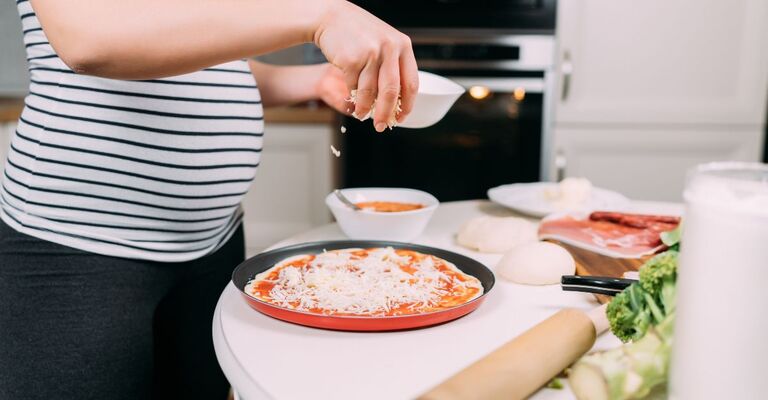 Donna incinta che cosparge la mozzarella sulla pizza