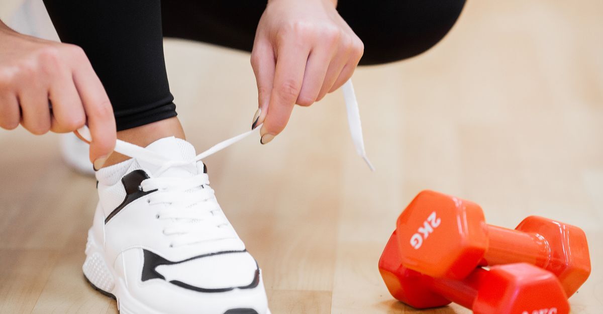 Una persona si allaccia le scarpe da ginnastica affianco a dei pesi