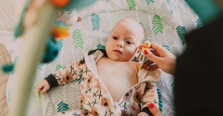 Mamma che misura la febbre a un neonato sdraiato
