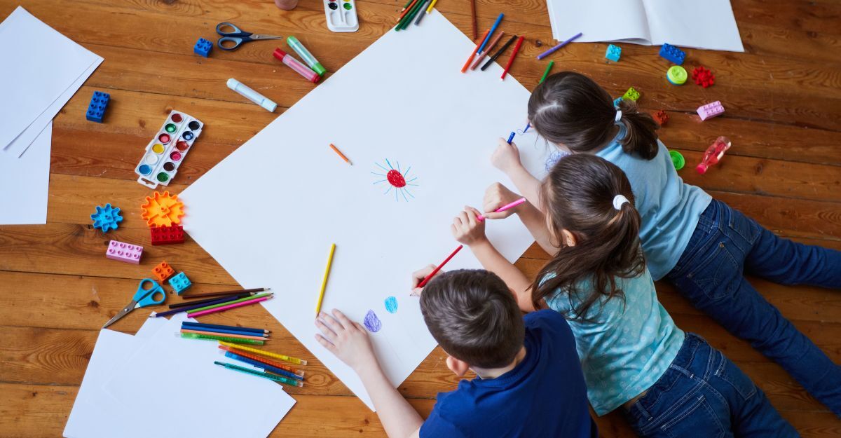 bambini pitturano su un foglio bianco sdraiati sul pavimento