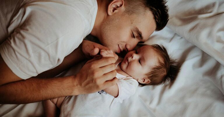 Papà che coccola la figlia neonata sul lettone