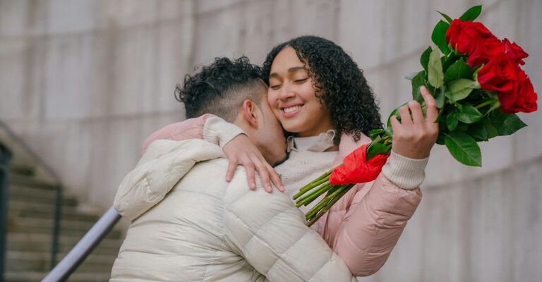 Coppia con ragazzo che stringe la fidanzata alla quale ha appena regalato un mazzo di fiori