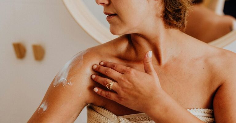 Donna con telo dopo la doccia che si applica una crema corpo