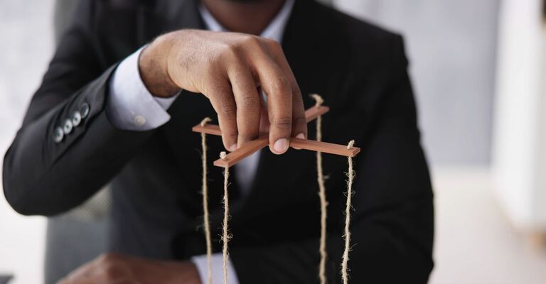 Un uomo che tiene tra le dita i fili di una marionetta