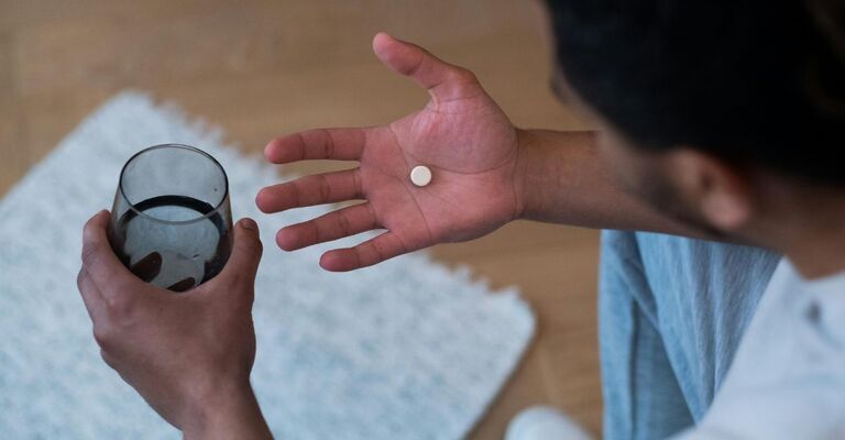 Focus di una mano con una compressa sopra e bicchiere d'acqua nell'altra