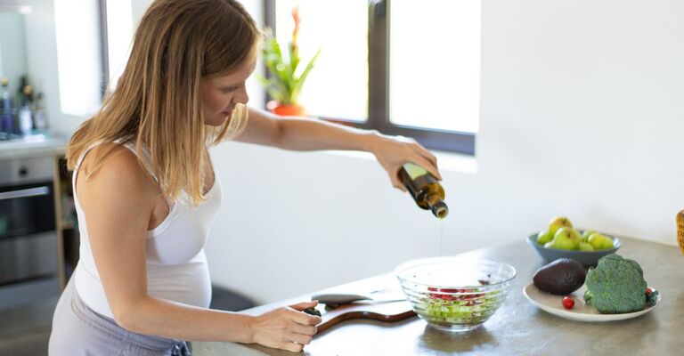 Giovane donna in cucina che aggiunge dell'aceto alla sua insalata