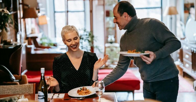 Un uomo serve i piatti in tavola per lui e la sua compagna in occasione di San Valentino