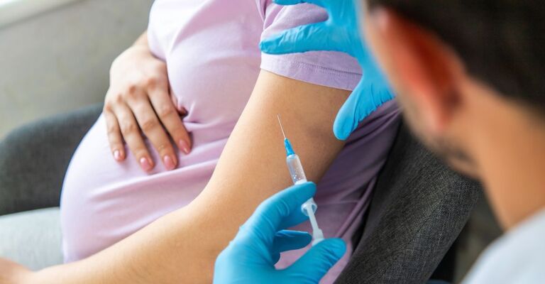 Primo piano su braccio di una donna incinta con dottore che esegue il vaccino con la siringa