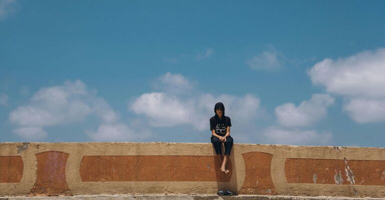 Un ragazzo da solo seduto su un muretto