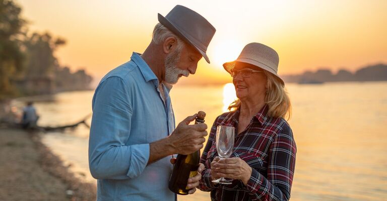 Una coppia festeggia l'anniversario con una bottiglia di spumante in riva al mare al tramonto