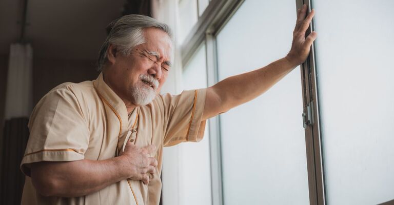 Un signore anziano appoggiato alla finestra si tiene il petto dolorante