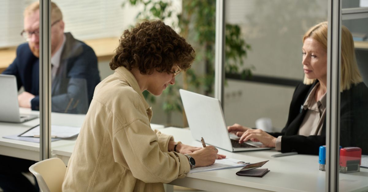 Ragazza che firma un foglio davanti a una dipendente amministrativa in un ufficio