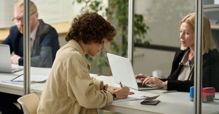 Ragazza che firma un foglio davanti a una dipendente amministrativa in un ufficio