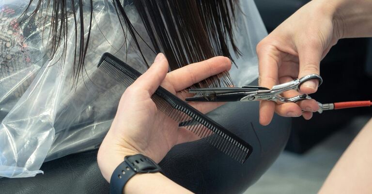 Mani di un parrucchiere che tagliano le lunghezze dei capelli di una cliente con pettine e forbici