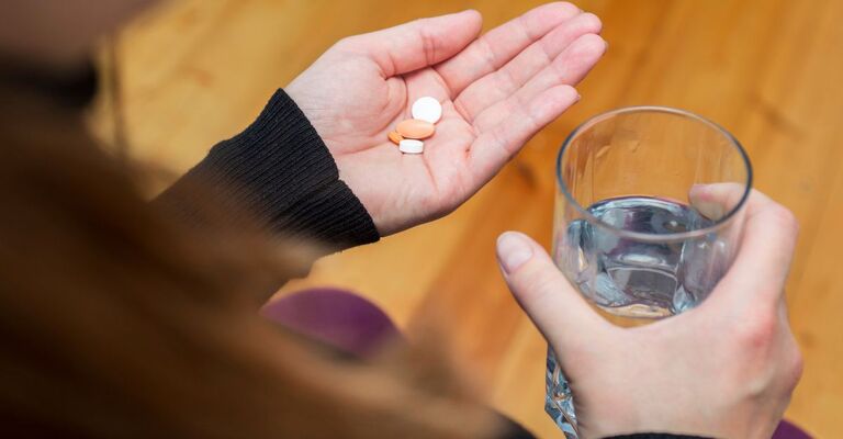 donna prende 2 pastiglie con un bicchiere d'acqua
