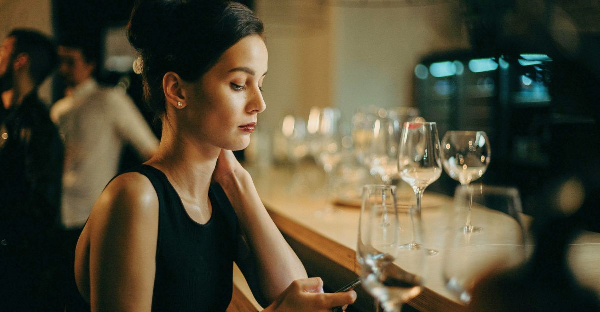 Giovane donna sola seduta al bancone di un bar mentre scrolla sul telefono