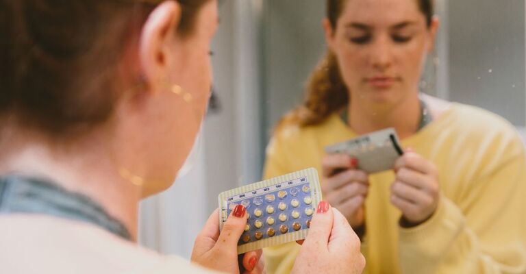 Una ragazza allo specchio con in mano un blister di pillola anticoncezionale