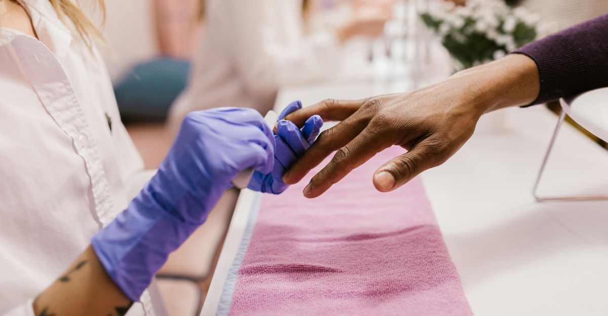 Onicotecnica che si prende cura delle mani e delle unghie della sua cliente con i guanti in salone