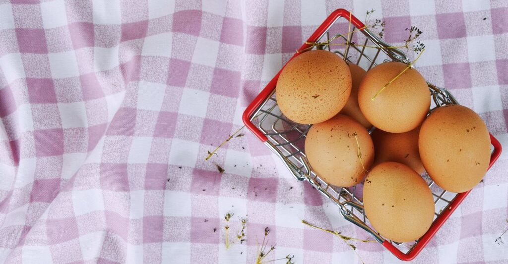 Uova in una cassetta sopra una tovaglia a scacchi lilla e bianca su un prato