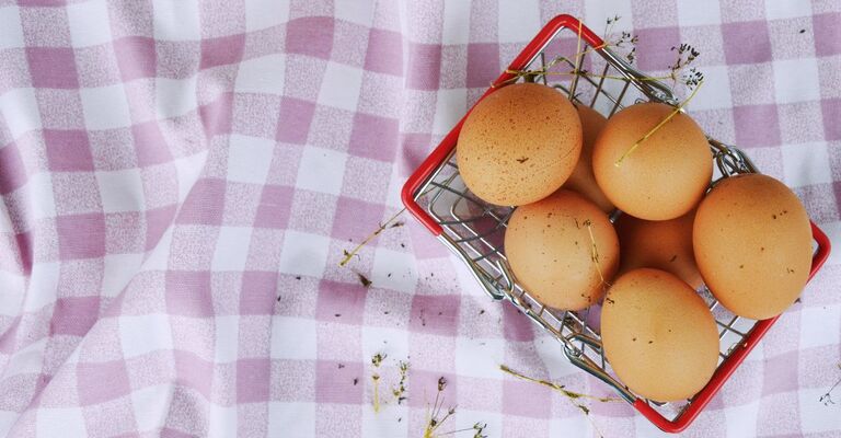 Uova in una cassetta sopra una tovaglia a scacchi lilla e bianca su un prato