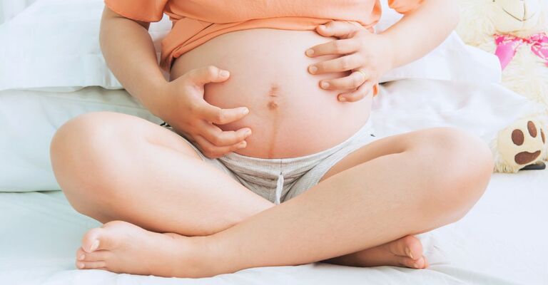 Donna incinta seduta a braccia incrociata che si gratta il pancione