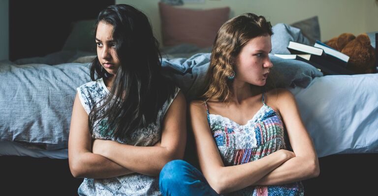 Due amiche arrabbiate sedute vicine a braccia conserte appoggiate a un letto