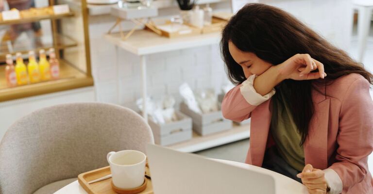 Ragazza che tossisce in un locale con braccio sulla bocca