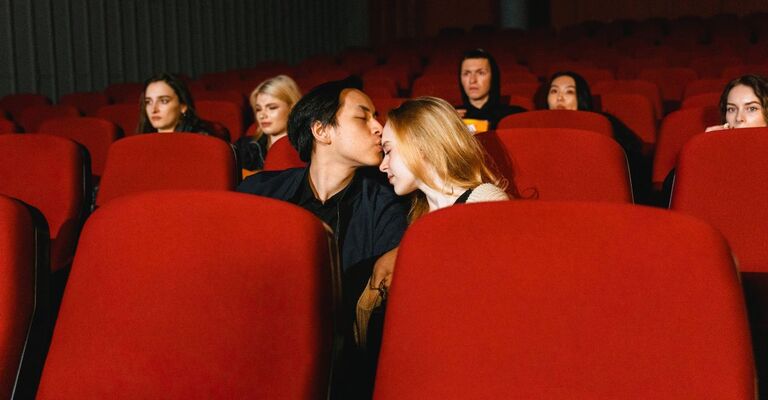 Una coppia seduta sulle poltrone rosse del cinema che si bacia durante la proiezione
