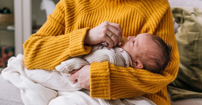 Mamma che culla il figlio neonato seduta sul divano e gli mette il ciuccio