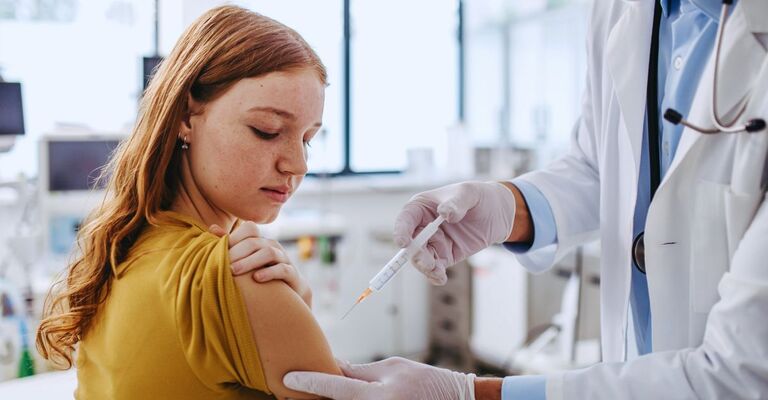 Medico somministra vaccino al braccio di una giovane ragazza coi capelli rossi