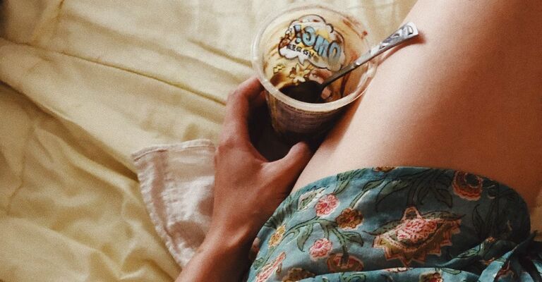 Una ragazza sdraiata a letto ha appena finito una vaschetta di yogurt