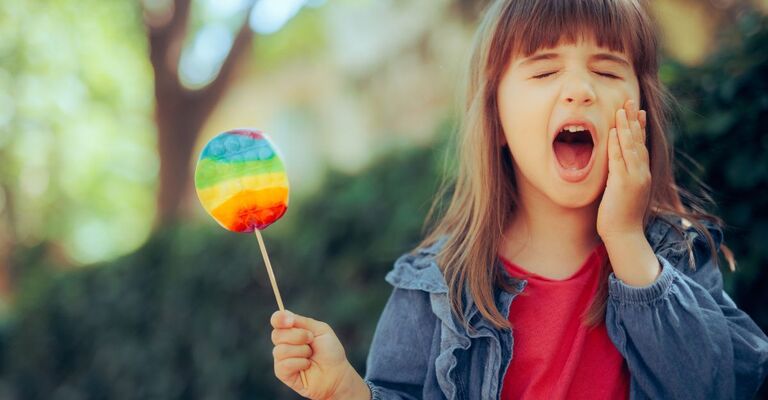 Una bambina si tiene la guancia dolorante e nell'altra mano ha un lecca-lecca