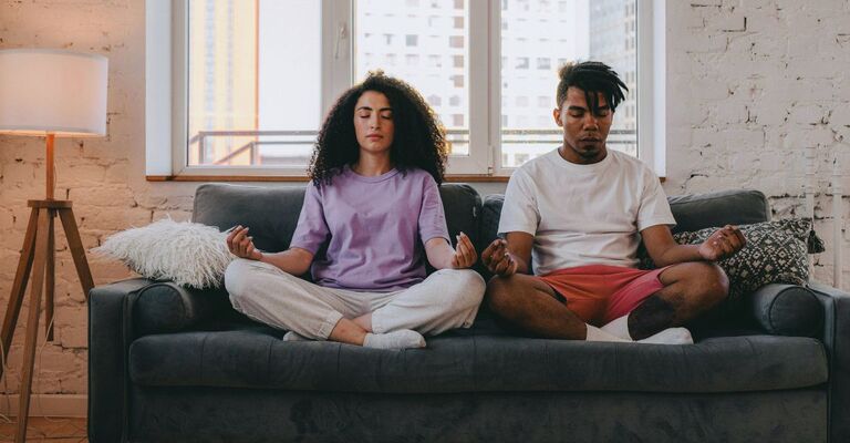 Un uomo e una donna sul divano che respirano a gambe incrociate