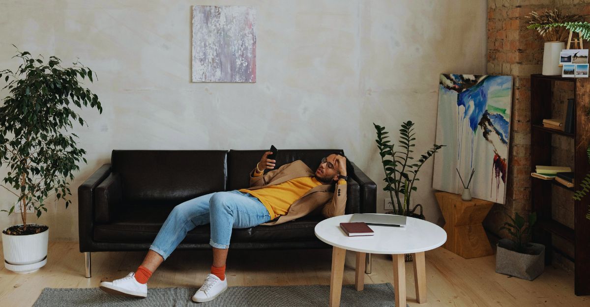 Uomo semi sdraiato sul divano che scrolla sul telefono mentre è annoiato