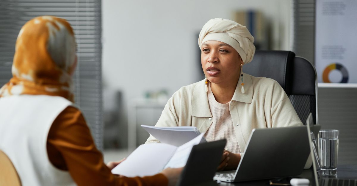 Donna con copricapo che parla con un'impiegata con dei fogli in mano